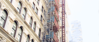 Scaffolding running up older building facade in Manhattan, NYC with newer buildings fading to white in the distance
