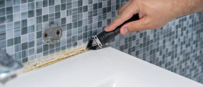 Plumber removes old dirty silicone from tub, cuts silicone adhesive with cutter