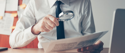 Businessman reading document contract papers with magnifying glass at office desk stock photo