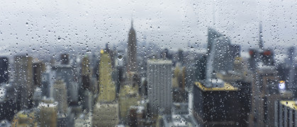 Panoramic view of New York City from behind of a wet window with the focus in the water drops on the glass. In background the blurred image of the city suggest a typical autumn day.
