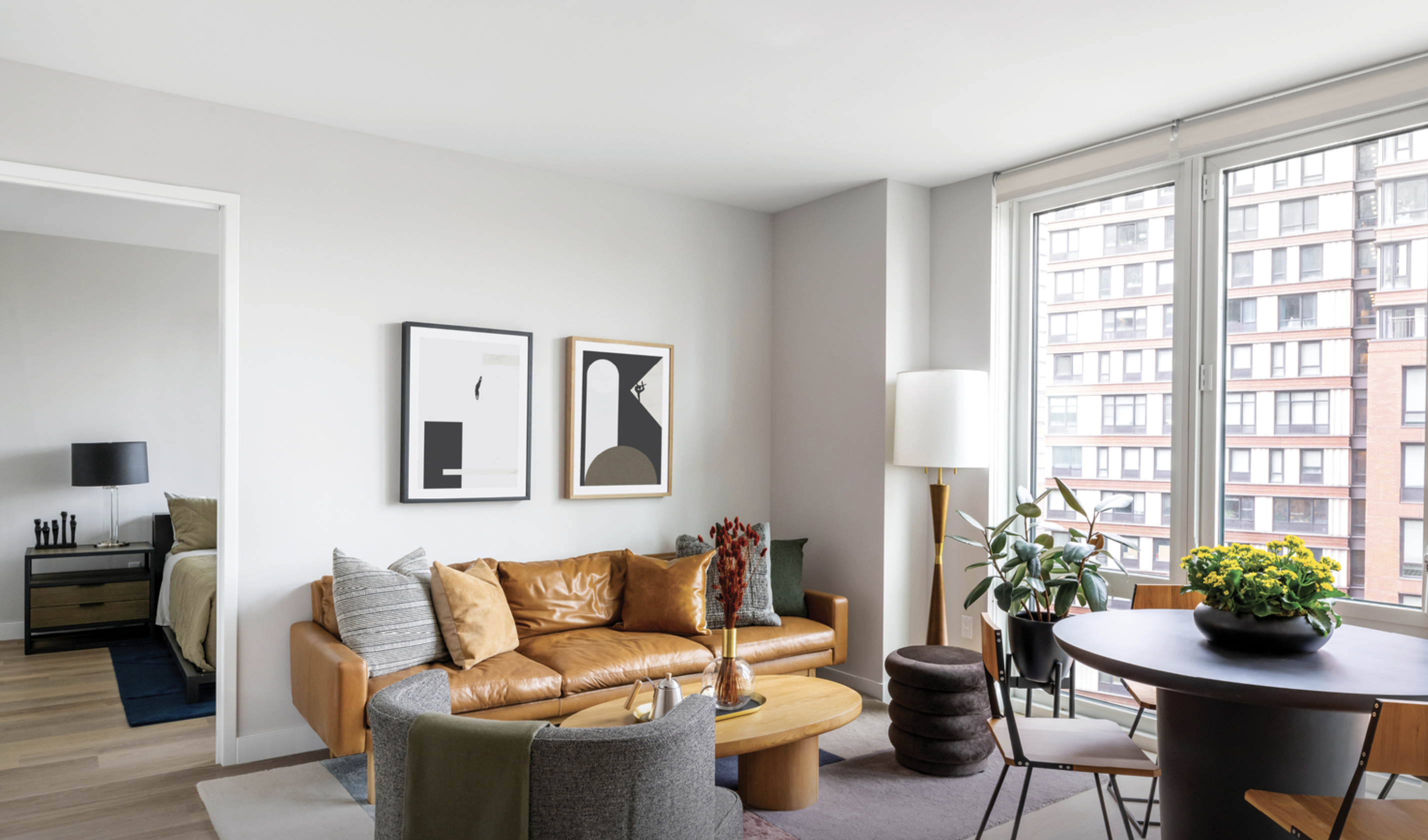 living room with brown leather sofa, white walls, & large windows looking out on another building