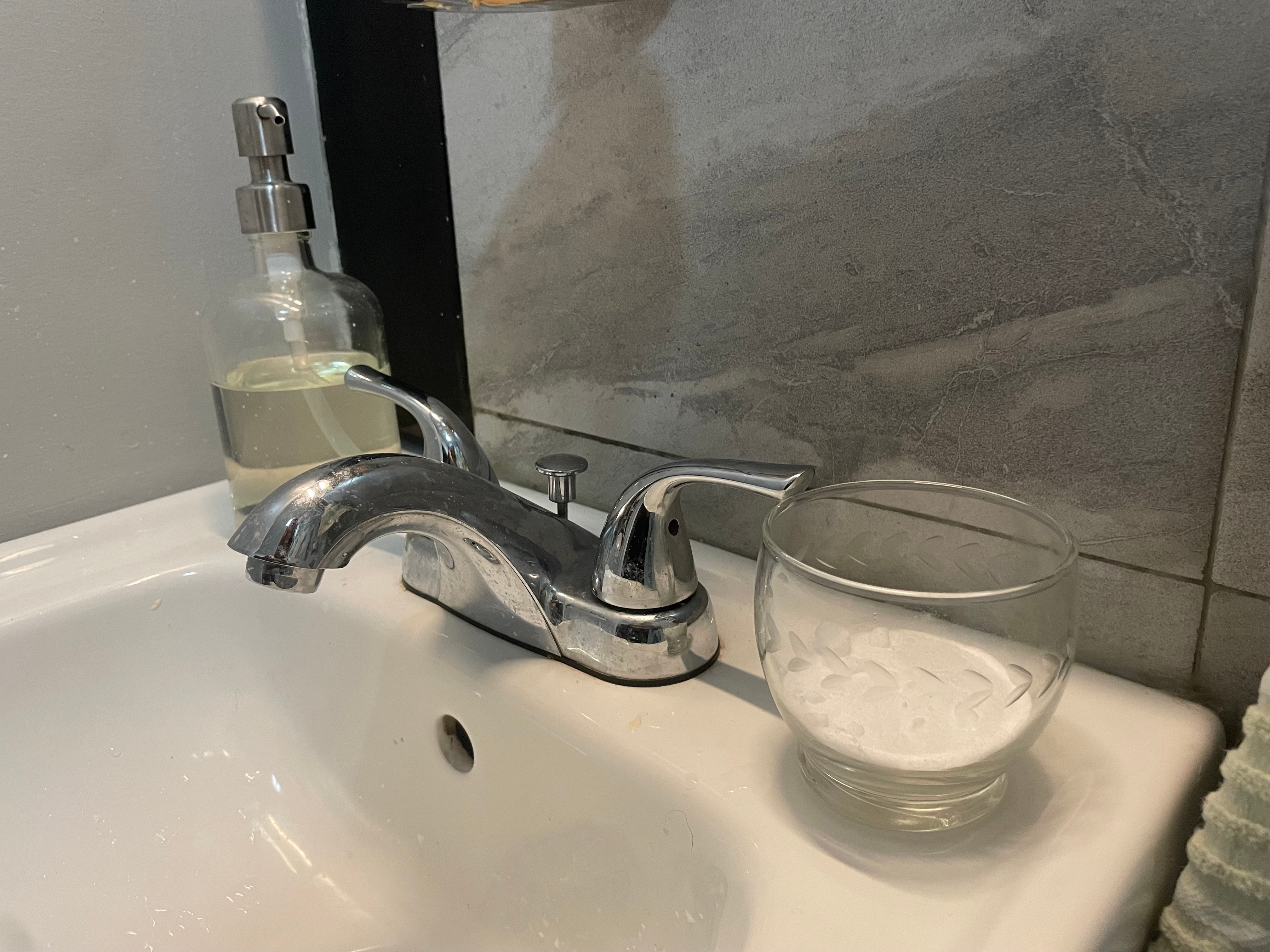 A cup of baking soda sits on a bathroom sink.