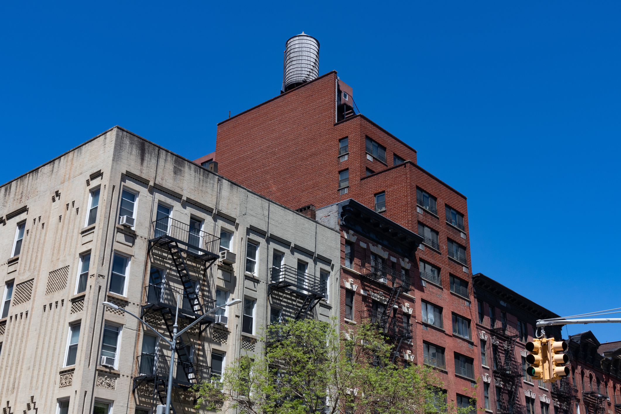 iStock-1337358591.jpg A row of colorful old brick apartment buildings with fire escapes along a street with a stop light on the Upper East Side of New York City