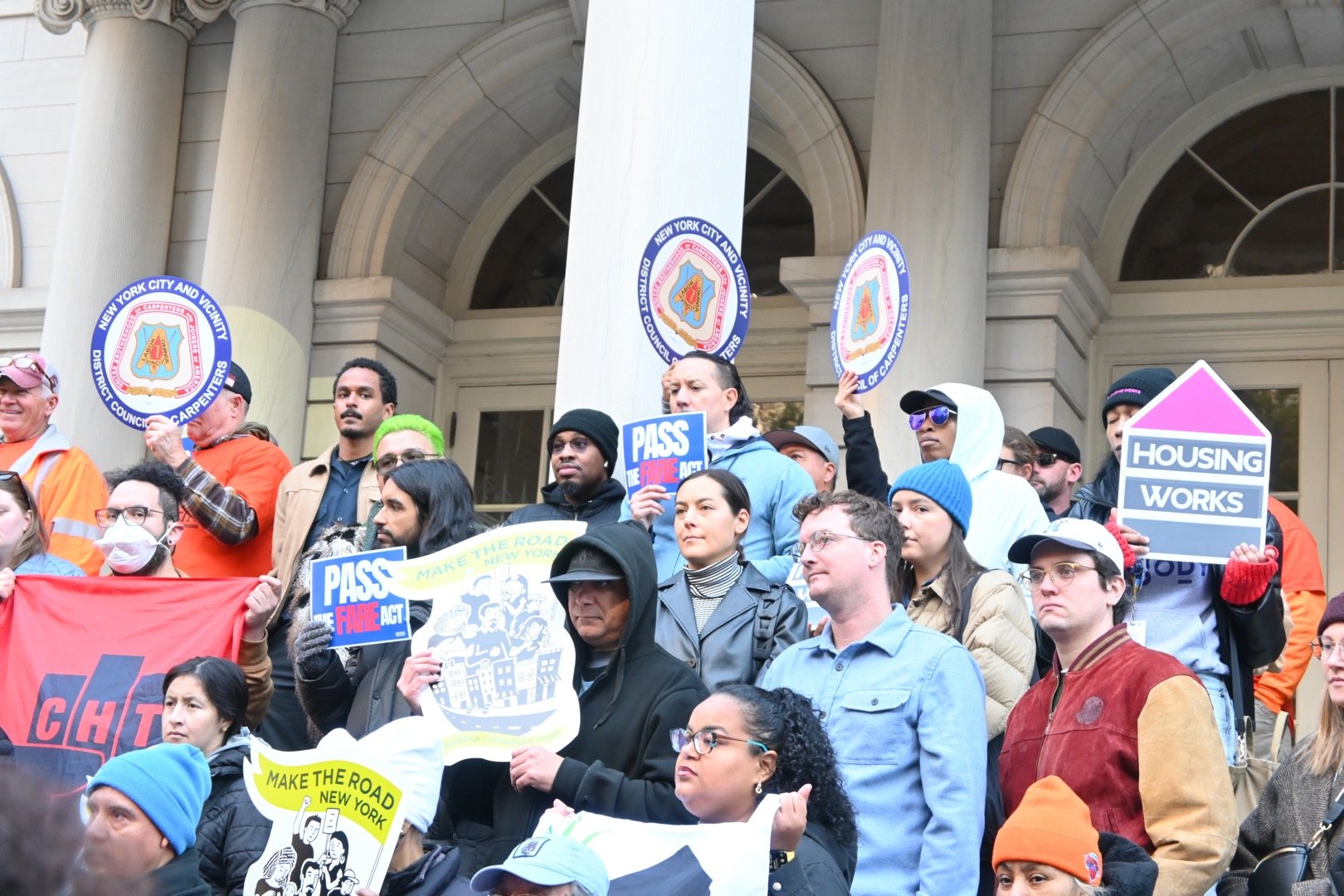 A group of supporters of the FARE Act hold up signs at a rally on the steps of city hall.