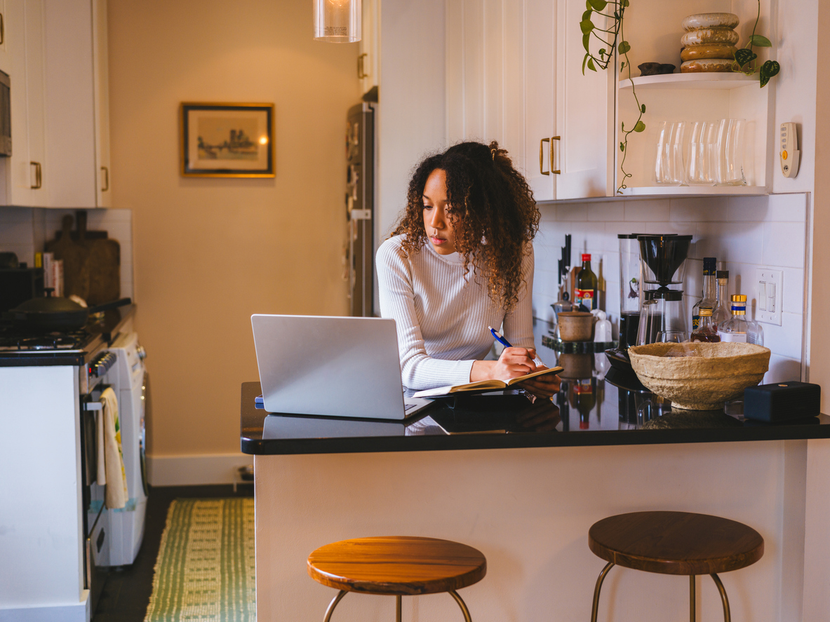 A young lady studying at the kitchen counter, utilizing a laptop and notepad.