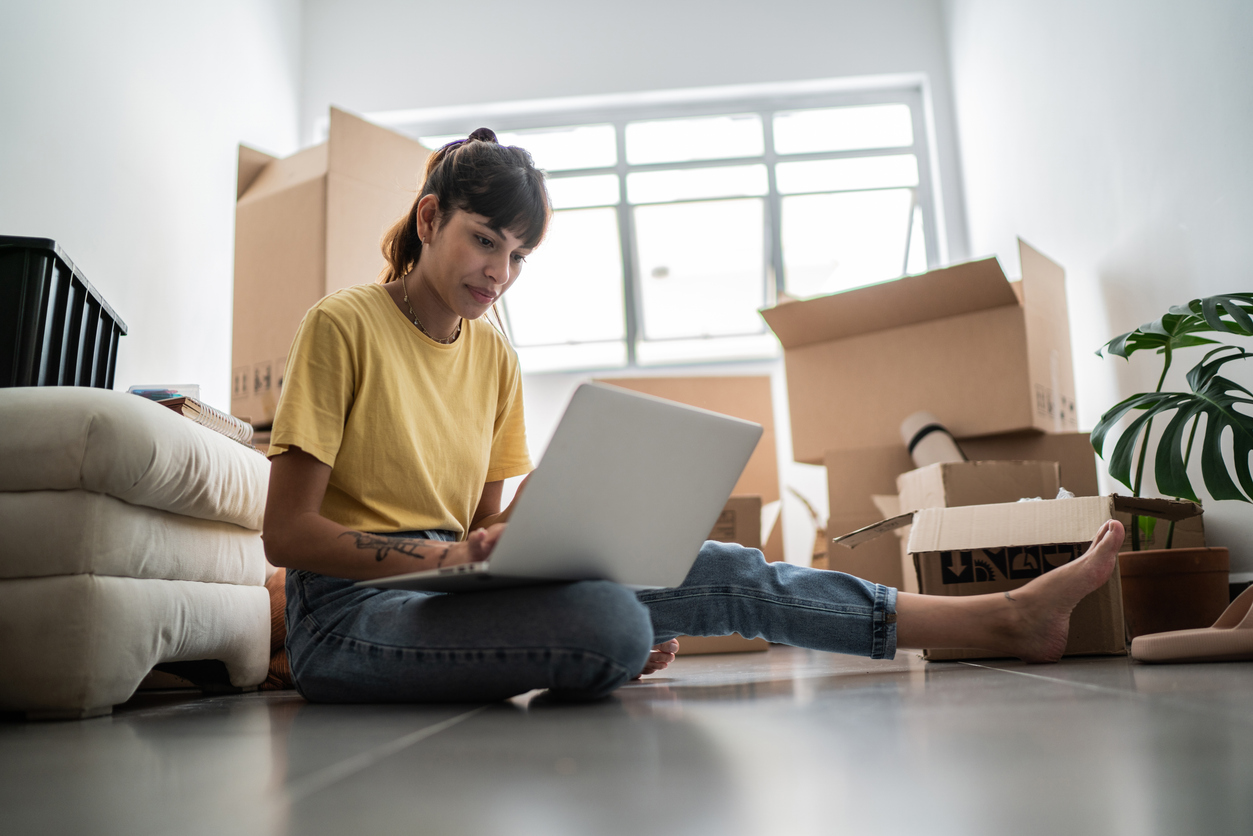Young woman using laptop at new apartment, with moving boxes around. Young woman using laptop at new apartment, with moving boxes around.