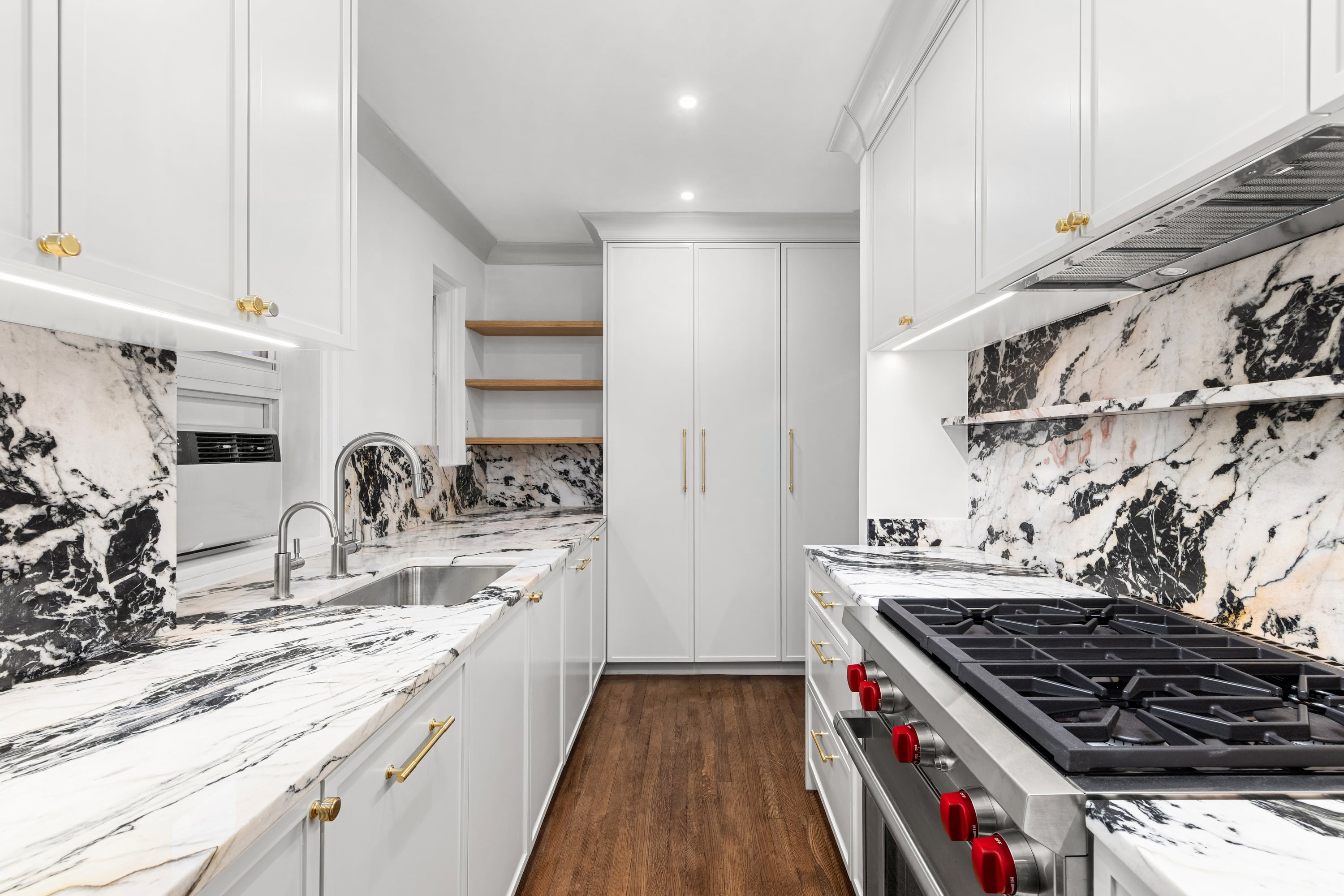 A new, white, marbled kitchen with stainless fixtures and striking red control knobs on the stove
