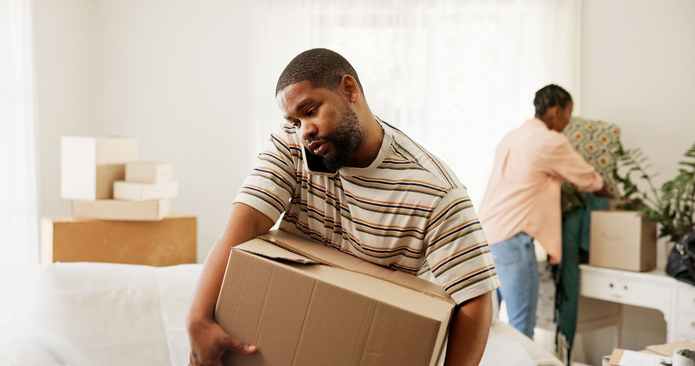 Man carrying a moving box in the middle of a move-prepped living room