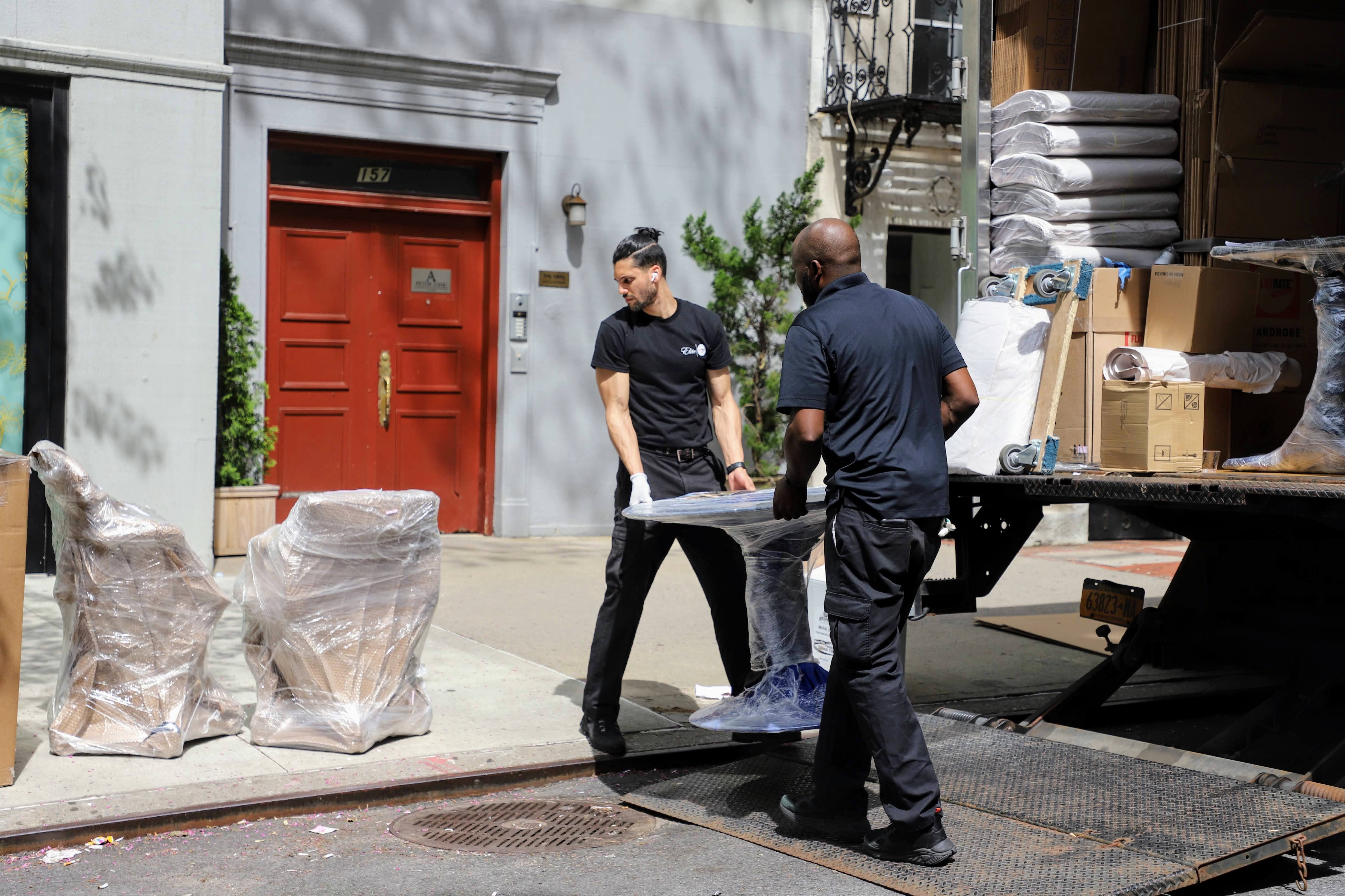 Movers loading shrink-wrapped furniture into a truck outside a New York City townhouse.