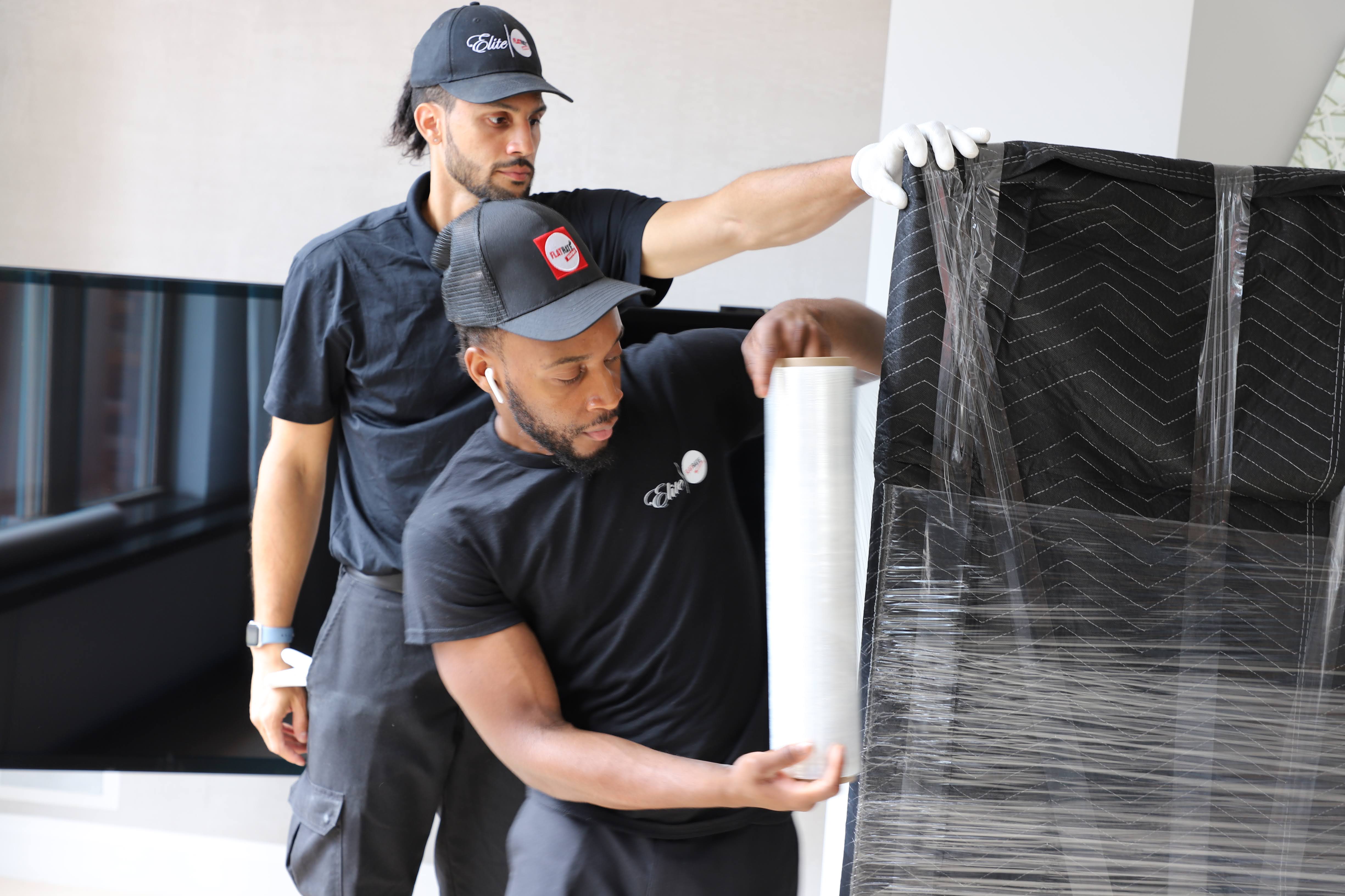 White-glove movers wrapping a large item in protective film before transport.