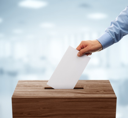 A disembodied hand puts a ballot in a voting box. A disembodied hand puts a ballot in a voting box.