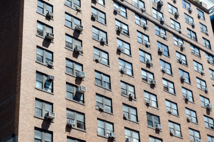 Tall apartment building with air conditioning machine at almost every window in New York city during summer day.