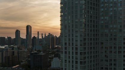 The Corporate Transparency Act requires NYC condo and co-op boards to file information about their beneficial owners with the U.S. Department of Treasury’s Financial Crimes Enforcement Network. Evening view of Hunters Point waterfront and Manhattan over the East River from a modern condo in Long Island City, Queens.