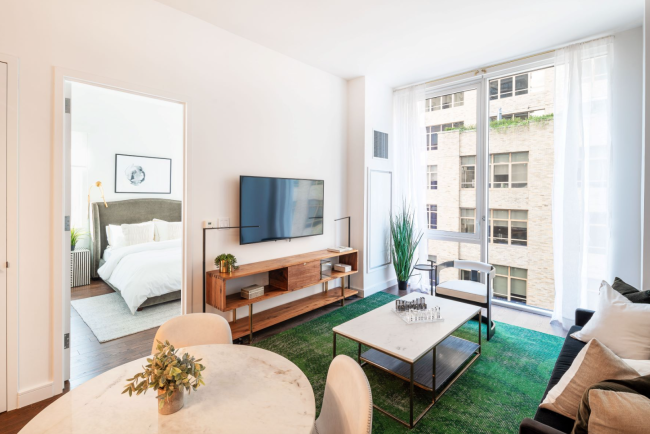 living room with brown sofa, green carpet, & large windows looking out on another Manhattan building