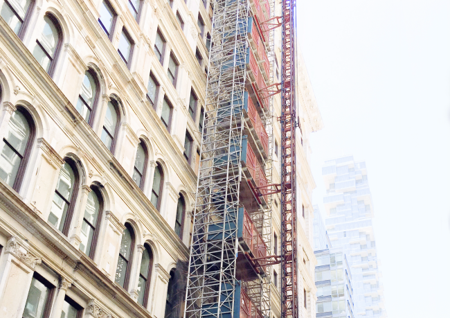 Scaffolding running up older building facade in Manhattan, NYC with newer buildings fading to white in the distance
