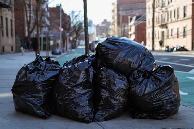 Black garbage bags filled with trash along the street and sidewalk in Astoria Queens of New York City