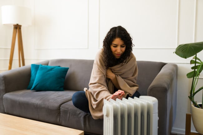 young woman using space heater to supplement apartment heat