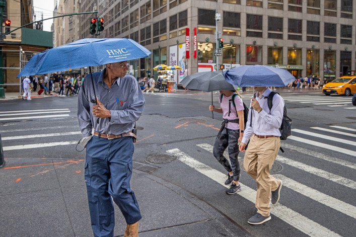 People with umbrellas crossing 5th Avenue