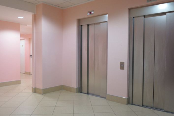 bank of 2 elevators at the base of apartment building lobby with pink walls