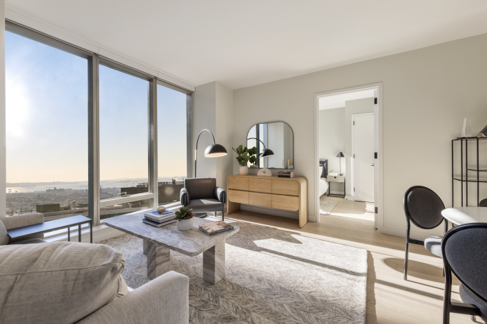 living room with sofa, white walls, & large windows looking out on NYC view