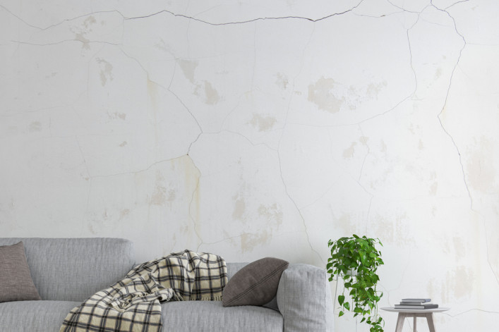 An apartment wall with cracks above a sofa.