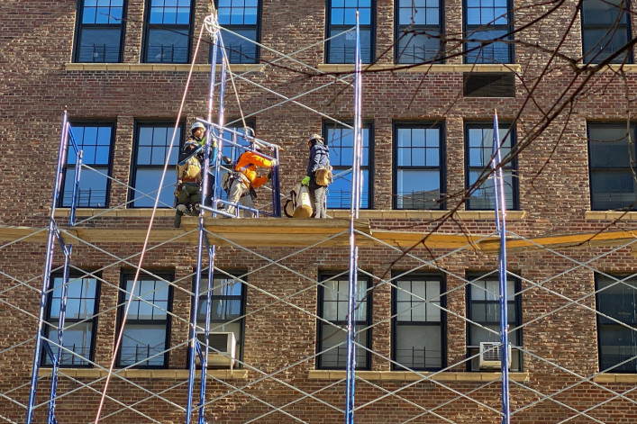 Four workmen in safety gear rig scaffolding in front of a Manhattan apartment building in 2022.