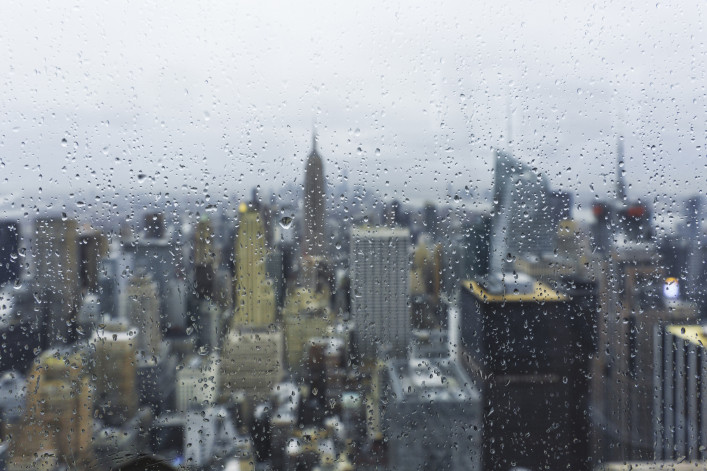 Panoramic view of New York City from behind of a wet window with the focus in the water drops on the glass. In background the blurred image of the city suggest a typical autumn day.