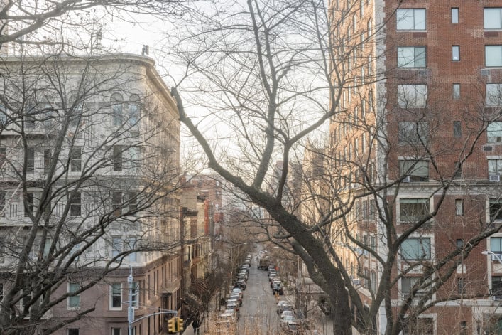 This is a photograph of a street in the Upper West Side in NYC viewed from the Summit in Central Park through bare tree branches.