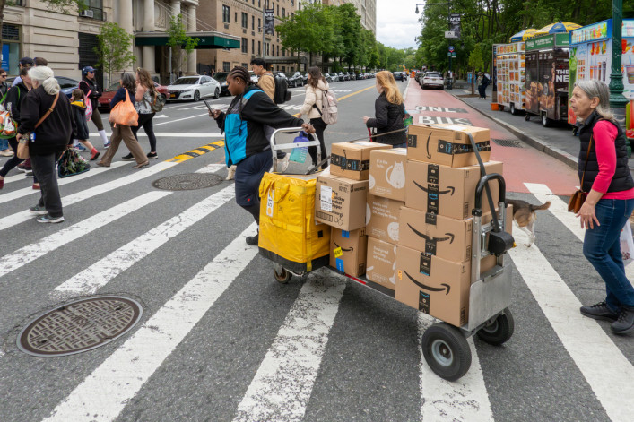 A driver pulls a trolley with Amazon Prime packages across a NYC street.