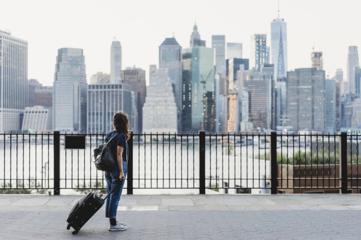 Woman with suitcase in Brooklyn looking over the East River at Manhattan