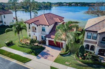 Overhead view of a large, sunny house with a water view behind it