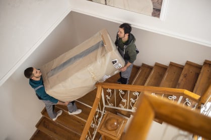 Two men moving a large box down a staircase