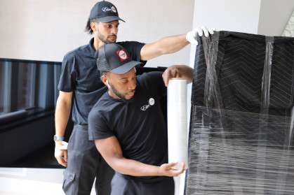 White-glove movers wrapping a large item in protective film before transport.