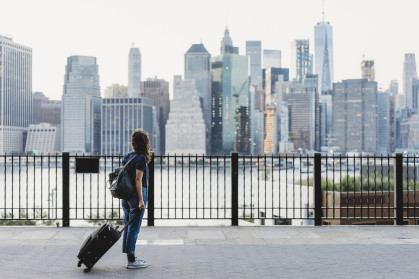 Woman with suitcase in Brooklyn looking over the East River at Manhattan