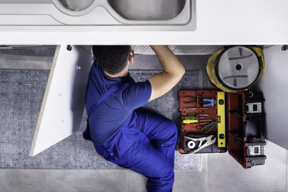 A plumber repairs a pipe beneath a sink