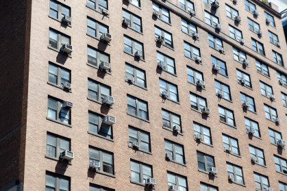 Tall apartment building with air conditioning machine at almost every window in New York city during summer day.