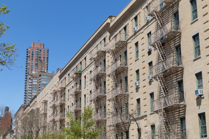 A row of similar old brick residential buildings with fire escapes on the Upper East Side of New York City