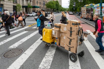 A driver pulls a trolley with Amazon Prime packages across a NYC street.