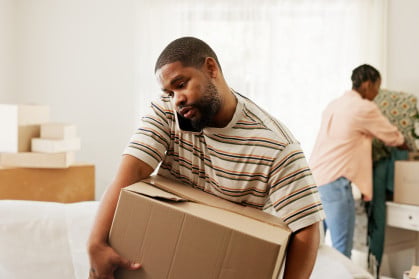 Man carrying a moving box in the middle of a move-prepped living room