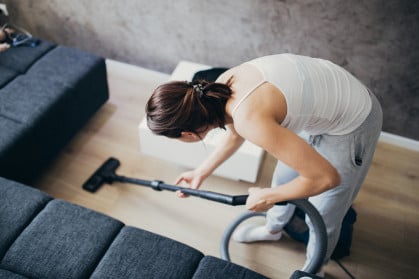 woman vacuuming the floor next to her couch