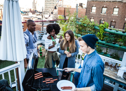 Friends having fun, grilling BBQ and drinking beers together during a rooftop party in New York East Village.
