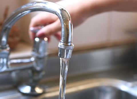 faucet with hand of woman in kitchen for cleaning, drinking and washing dishes. Interior, steel and household plumbing with sink and tap at home for stream, flowing and splash