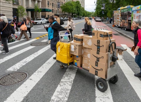 A driver pulls a trolley with Amazon Prime packages across a NYC street.