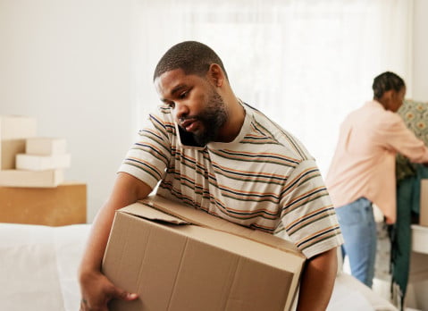 Man carrying a moving box in the middle of a move-prepped living room