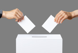 Two hands about to drop ballots into a voting box on a grey background.