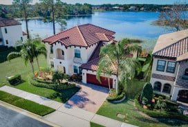 Overhead view of a large, sunny house with a water view behind it