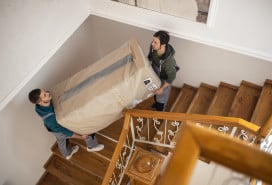 Two men moving a large box down a staircase