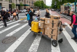 A driver pulls a trolley with Amazon Prime packages across a NYC street.