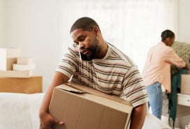 Man carrying a moving box in the middle of a move-prepped living room