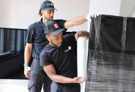 White-glove movers wrapping a large item in protective film before transport.